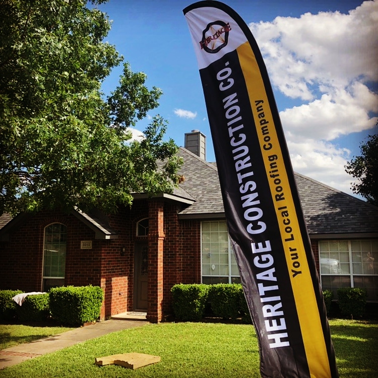 Heritage Construction feather flag in front of a Texas home mid-install